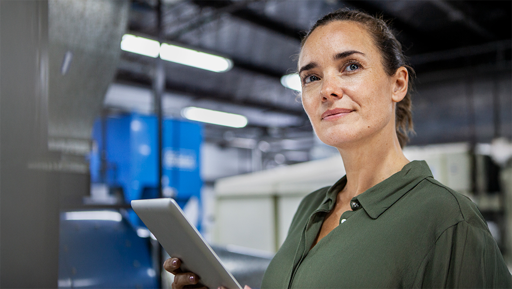 A woman smiling holding a tablet on the background of an industrial factory